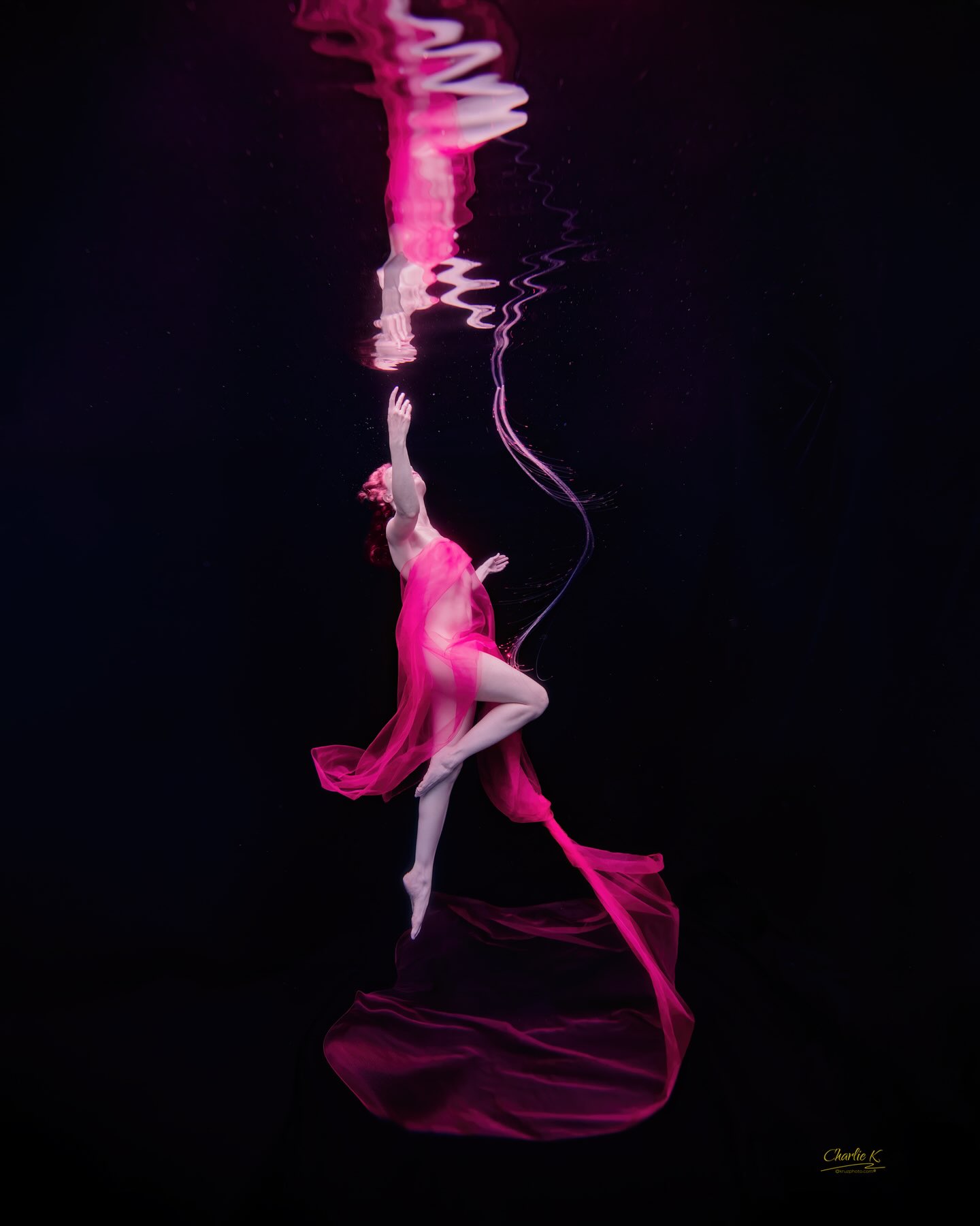 Figure in magenta silk reaching toward the surface in dark water